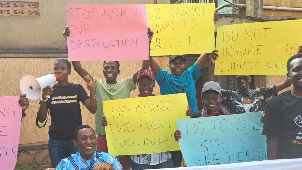Young people in Uganda holding placards including "Stop Insuring Our Destruction" and "Do Not Insure the Climate Crisis"